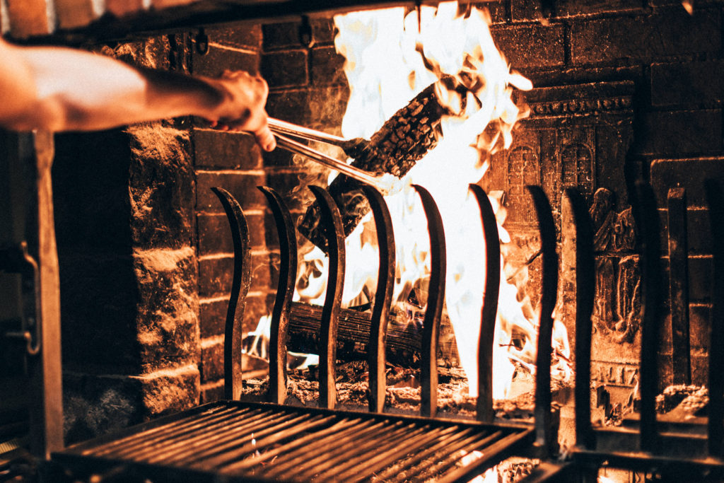 Personne ajoutant une bûche à l'aide d'un tisonnier dans un restaurant gastronomique avec feu de cheminée à Obernai